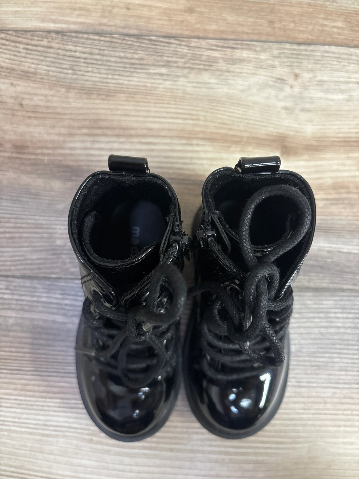 Shiny black toddler lace-up boots on wooden floor, children's footwear top view
