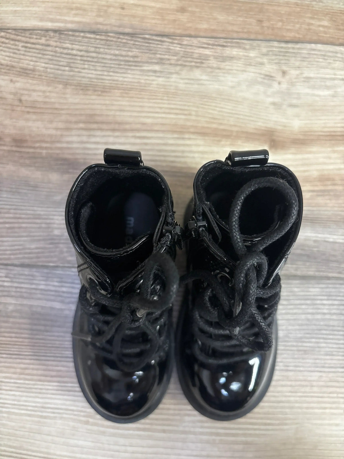 Top view of Steve Madden JPose black patent combat boots 7C showing lace-up front, side zipper and pull tabs on wood floor