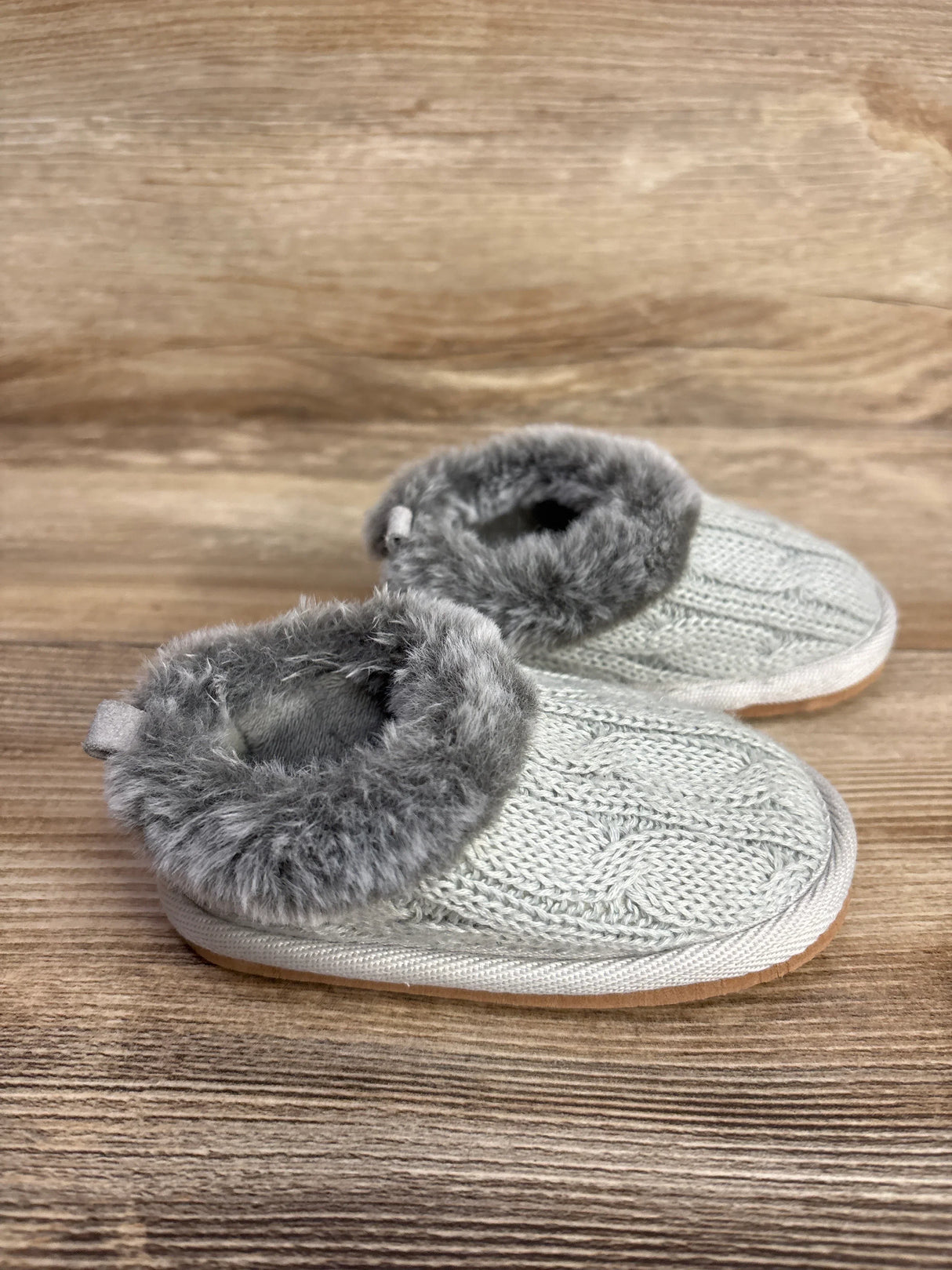 Gray knit baby booties with faux fur trim on a wooden surface