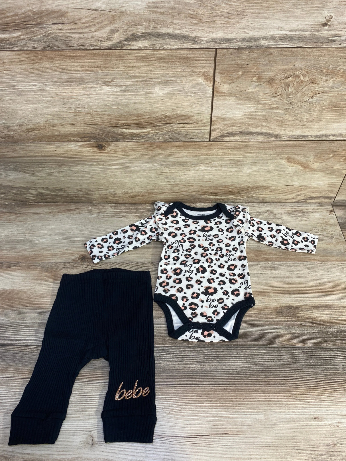 Leopard print baby onesie with black bebe pants on wood floor, newborn clothing set