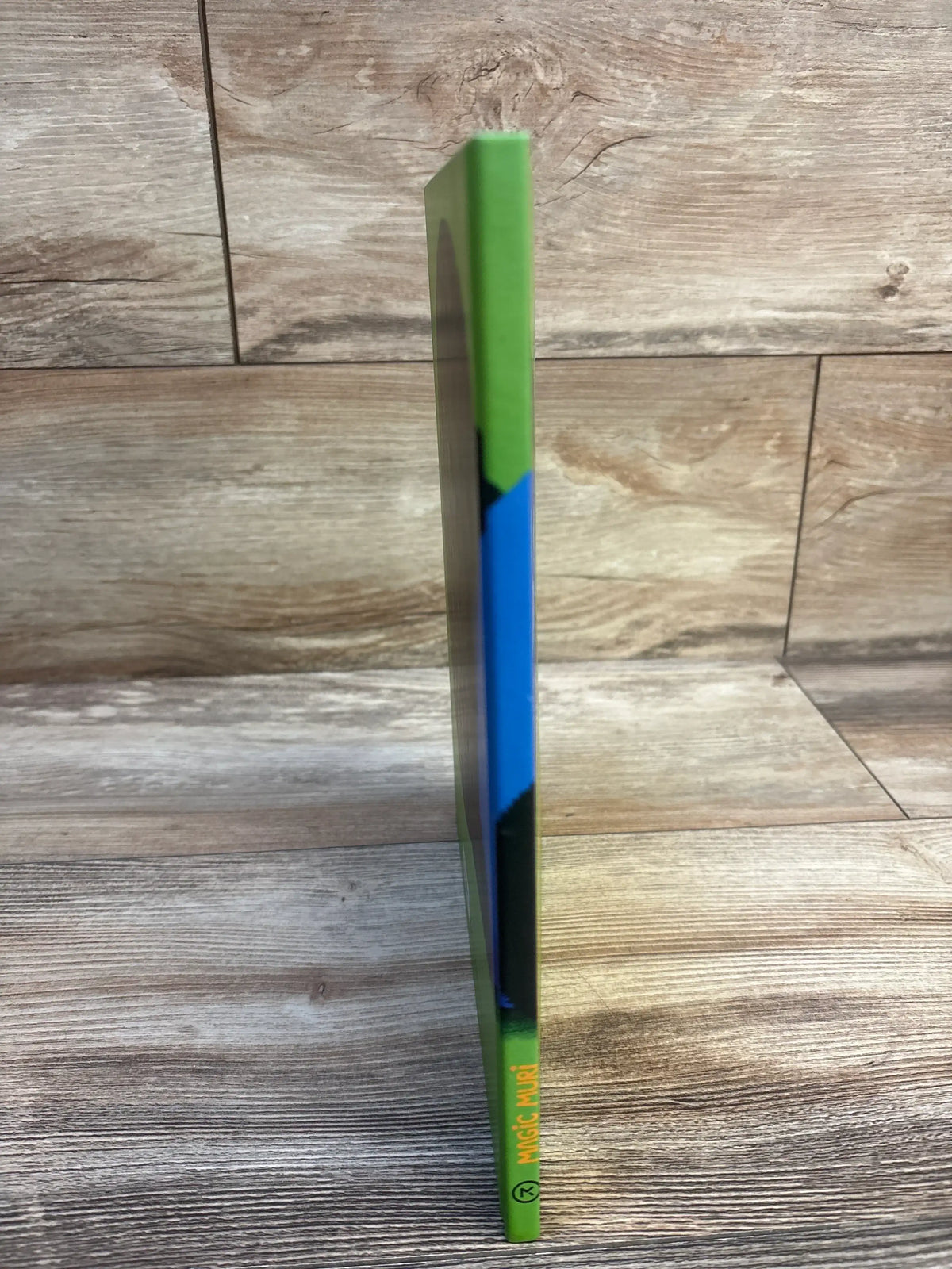 Magic Muri kids book with green and blue spine, standing on wood floor