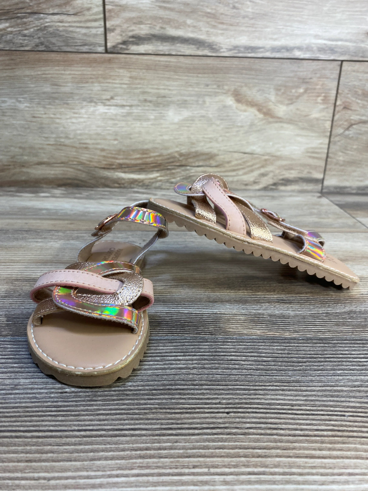 Girls’ metallic pink and gold sandals with iridescent straps on wood floor