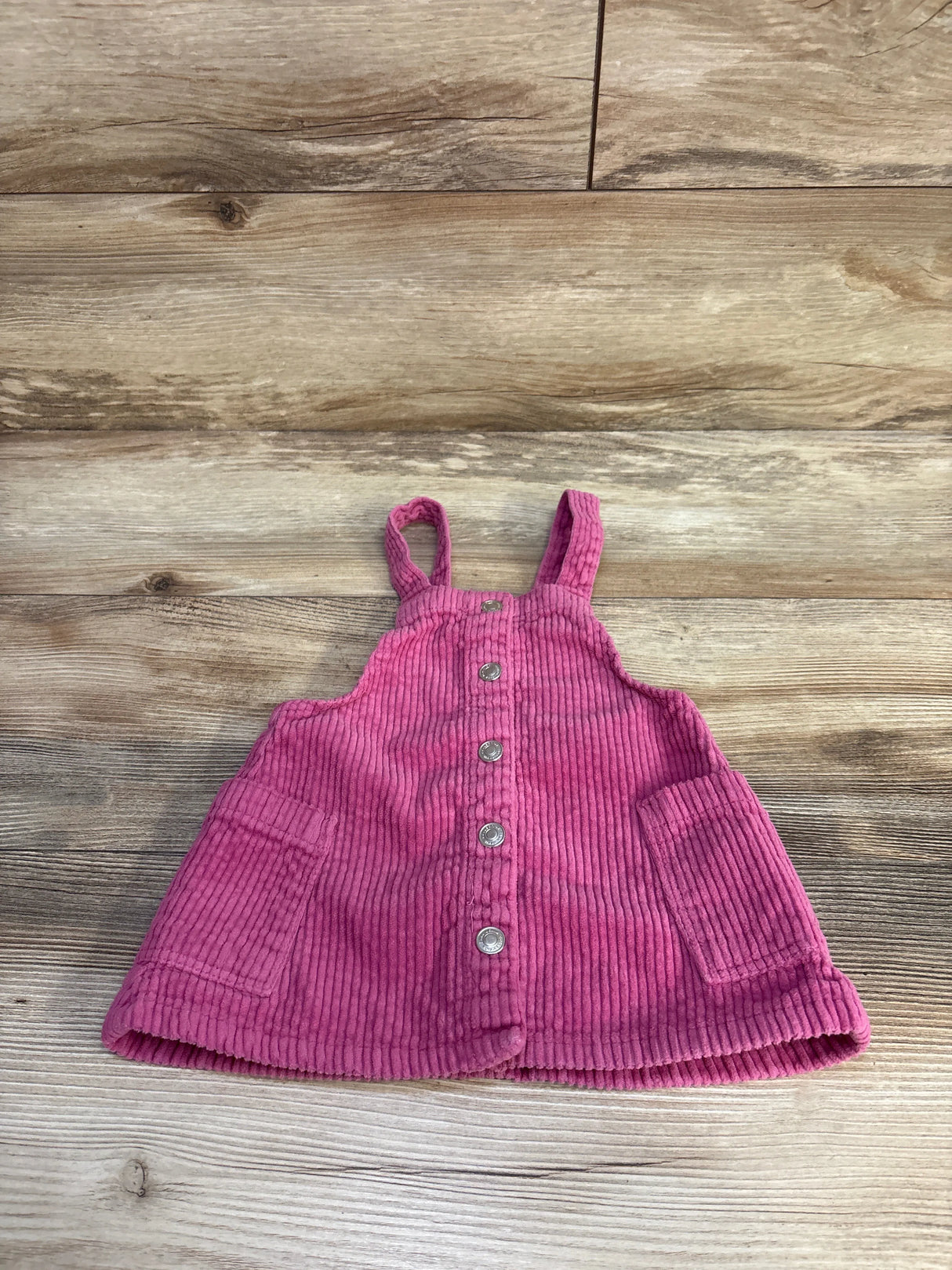 Front flat lay of pink Zara corduroy skirtall showing button front, two patch pockets and shoulder straps on wood background