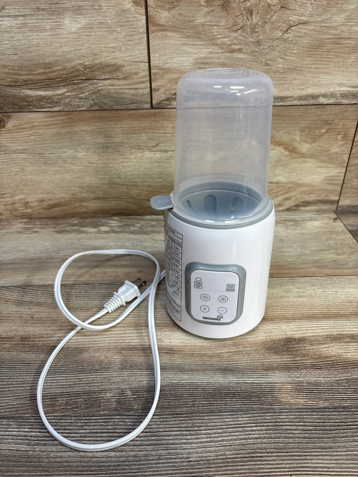Front view of Grownsy Baby Bottle Warmer, White with clear warming chamber, control panel, and cord on a wood surface