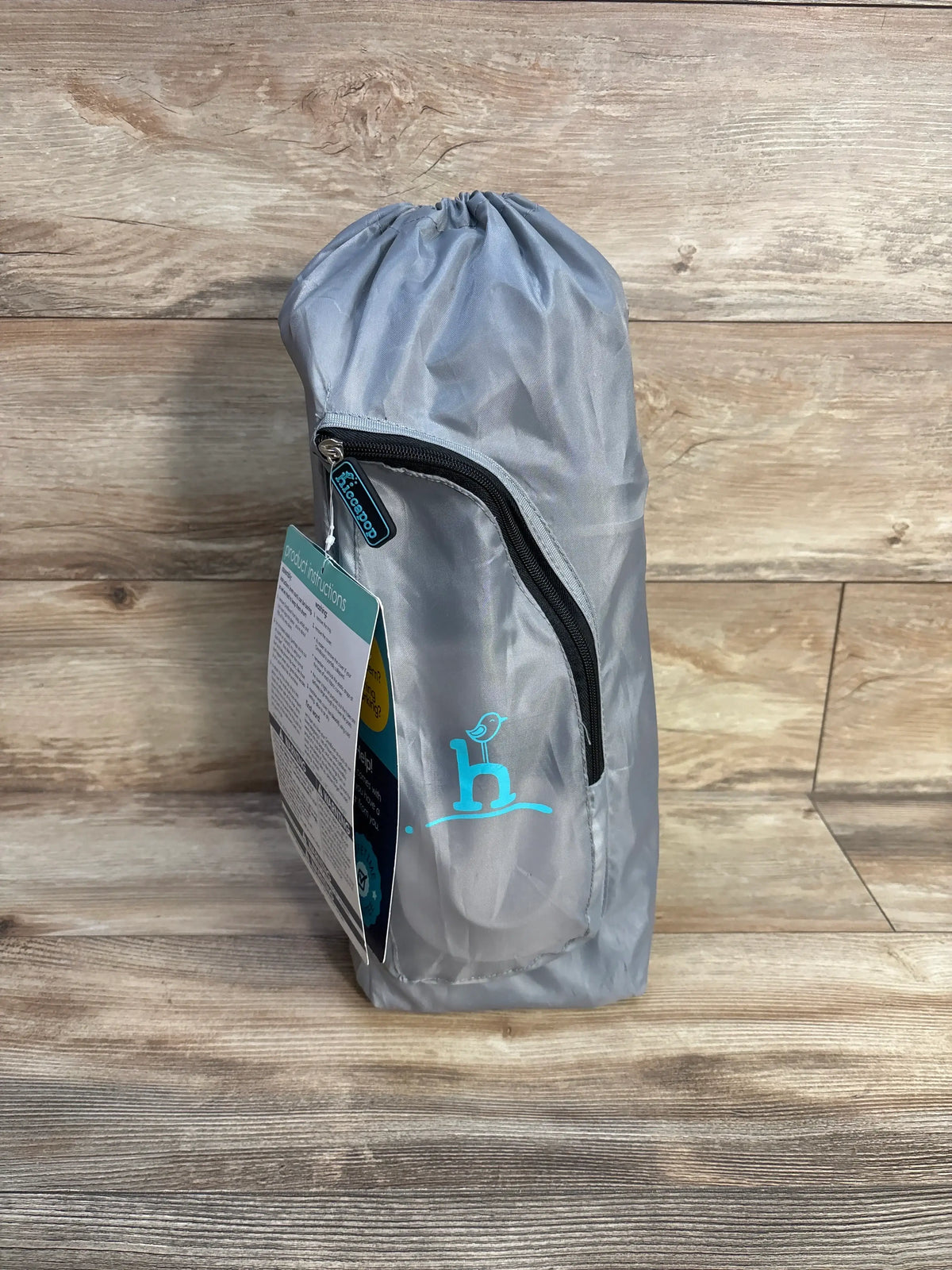 Front view of Hiccapop OmniBoost Folding Booster Chair in Gray carry bag with zippered pocket on wood-look floor