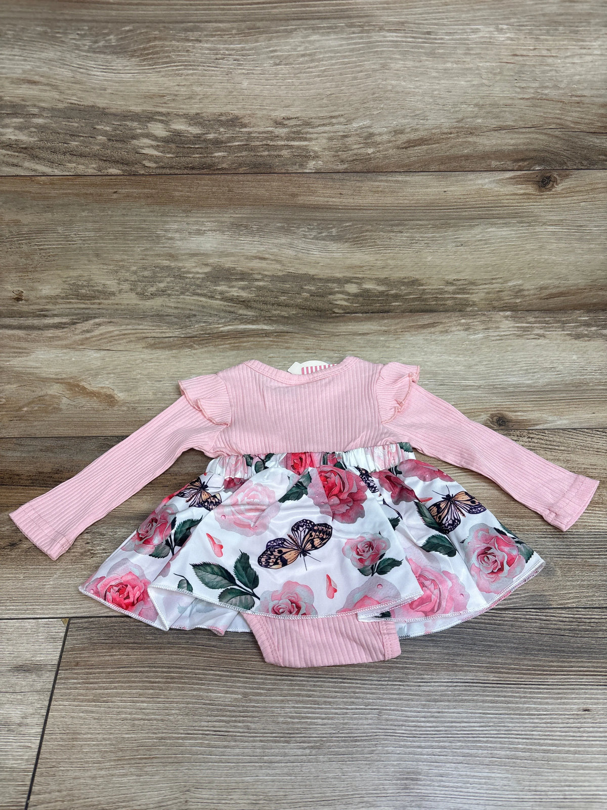 Flat lay of pink faux-suspender bodysuit dress showcasing long sleeves, ribbed fabric, floral butterfly skirt on wood