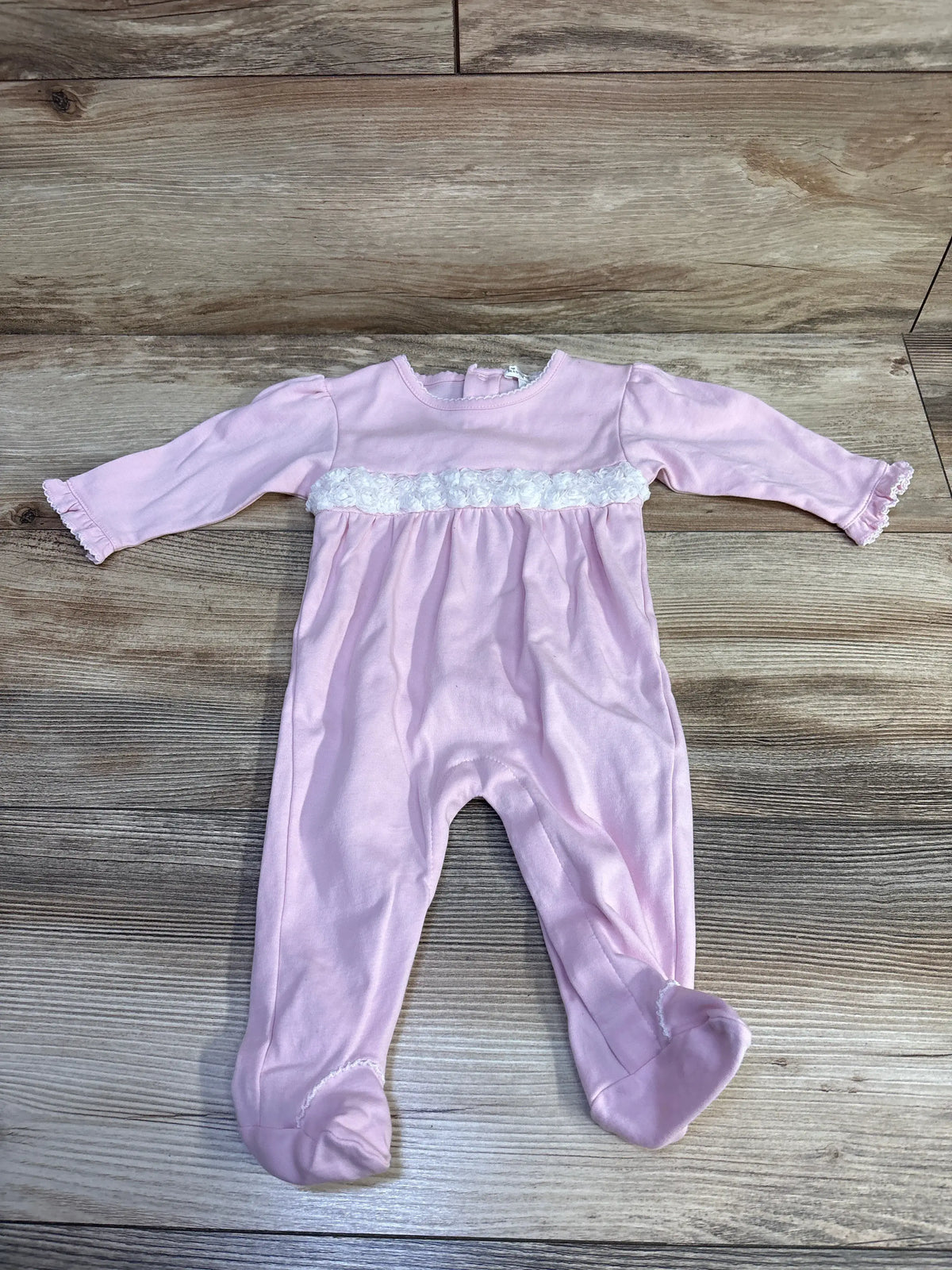 Front view of pink Kissy Kissy footie with long sleeves, enclosed feet, and white ruffle band on wood-look background