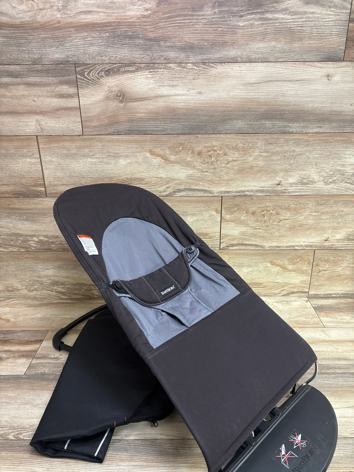 Angled view of BabyBjörn Balance Soft Bouncer in black and dark grey showcasing its padded seat and safety harness on a wood-look floor