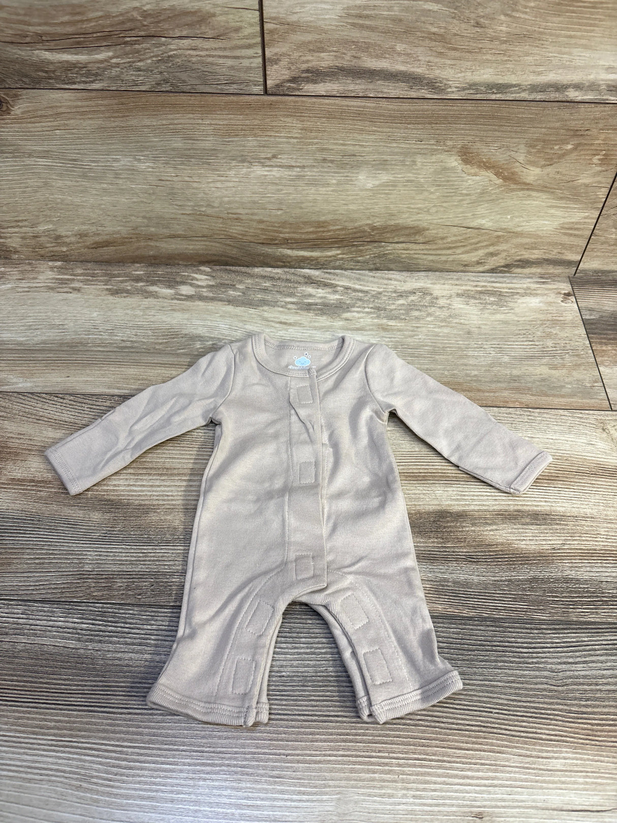 Top-down view of tan preemie coverall with front hook-and-loop closure and long sleeves on wood background