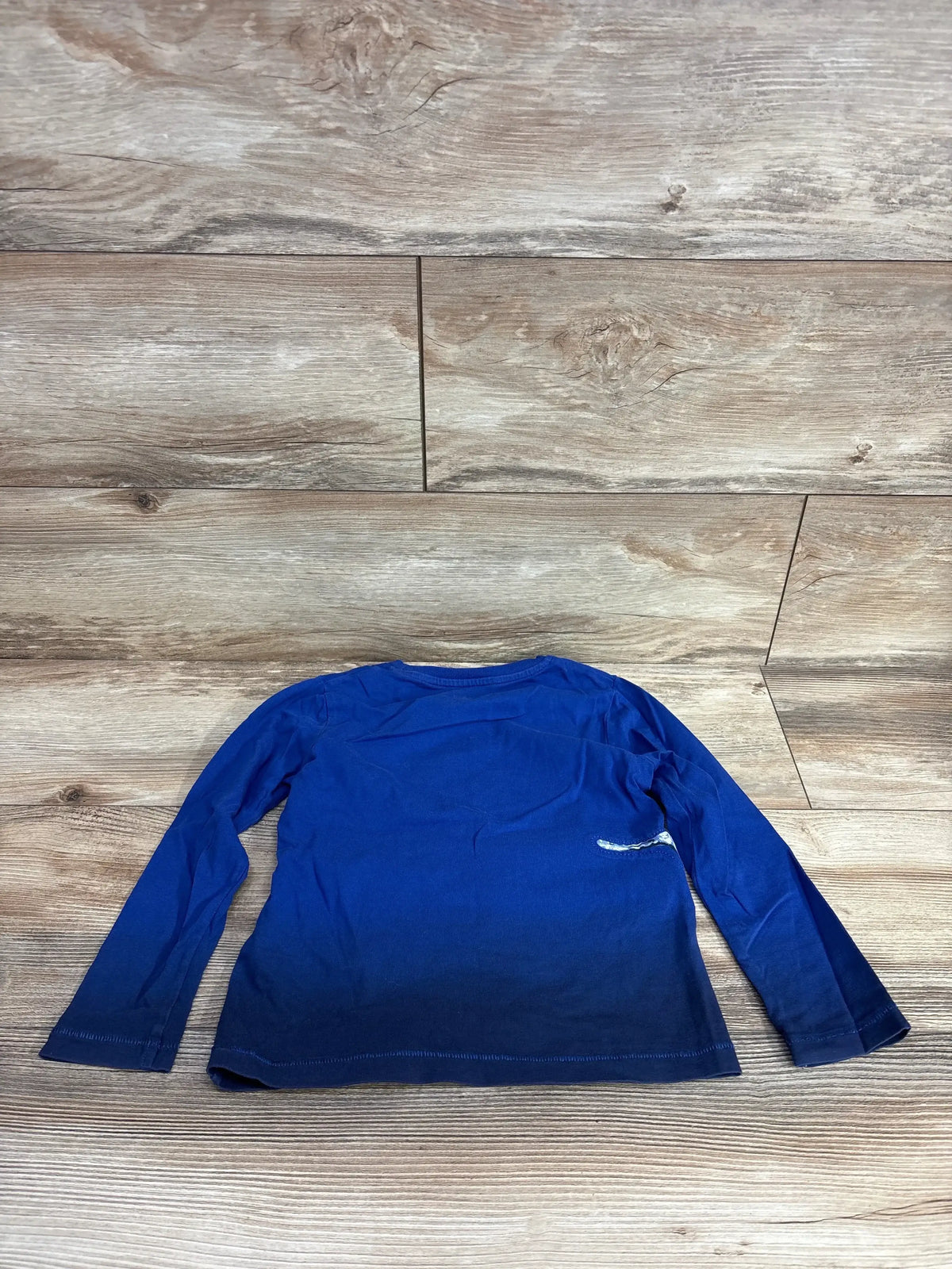 Blue ombre long sleeve kids shirt laid flat on wood floor background