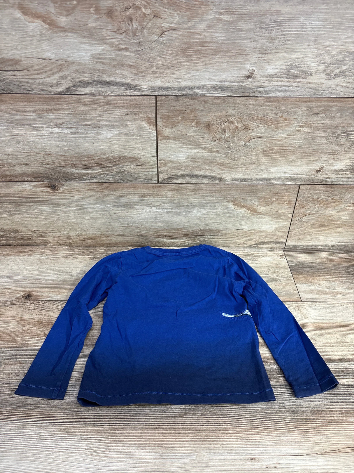 Blue ombre long sleeve kids shirt laid flat on wood floor background