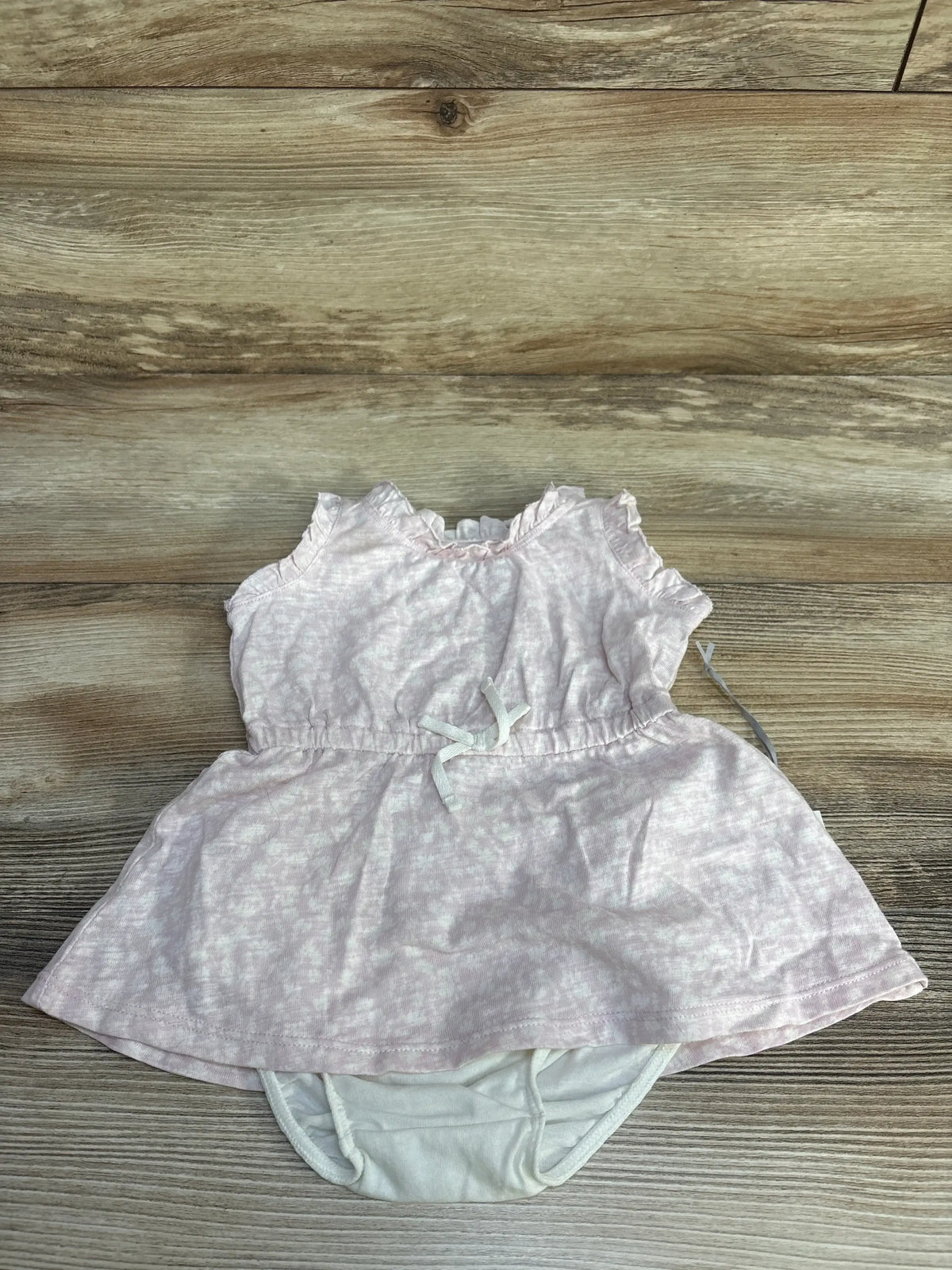 Front view of newborn light lilac floral dress with attached diaper-style bottom and small waist bow on wood plank background