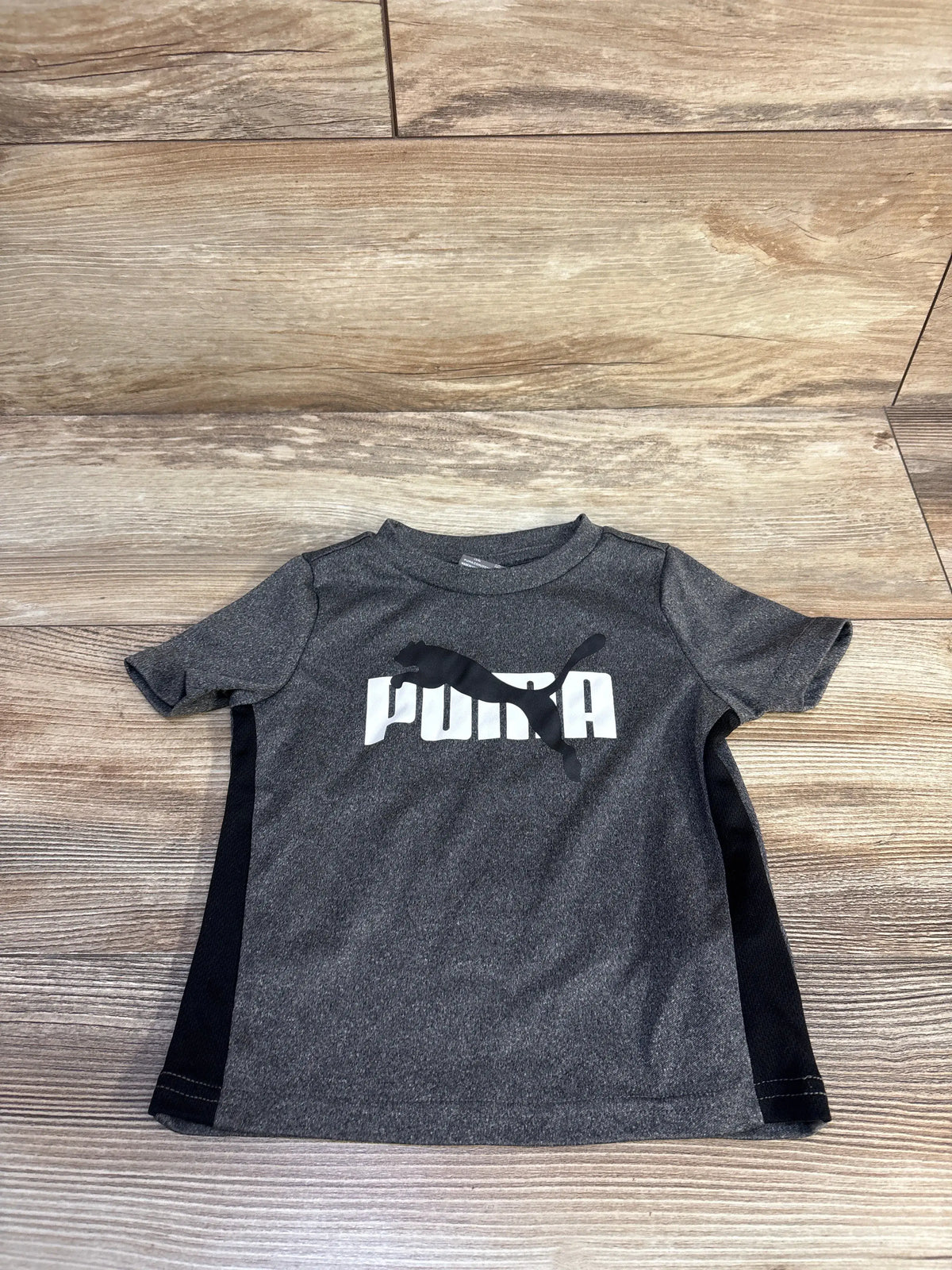 Grey Puma baby t-shirt with white logo and black side panels on a wooden background