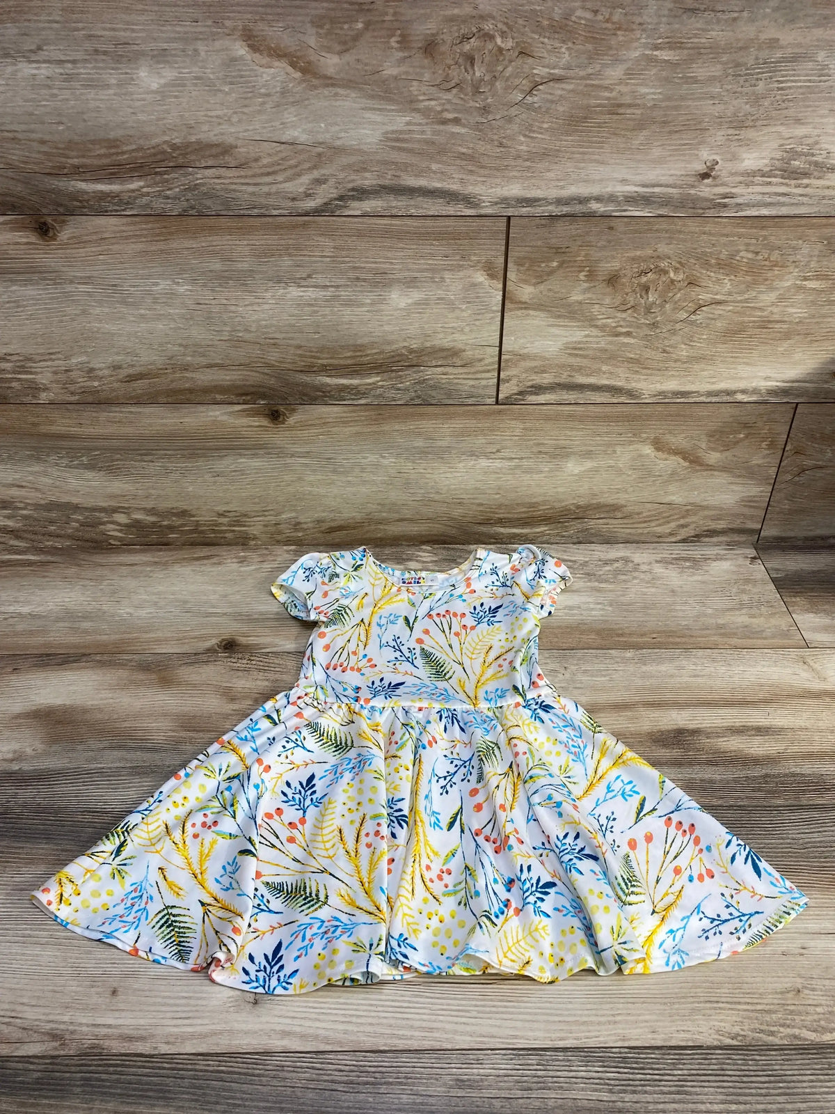 Flat lay of toddler twirl dress in white with multicolored floral and leaf print, cap sleeves and full skirt on wood background