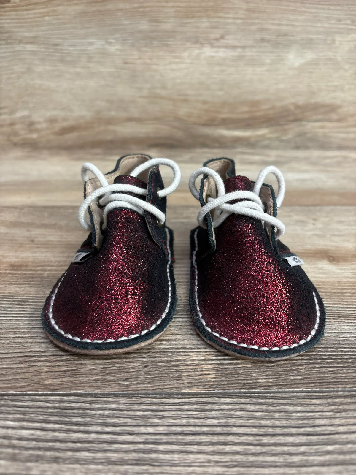 Front view of Monkey Feet lace-up glitter boots, red size 3/4C showing glitter uppers, white laces, and stitched sole on wooden floor