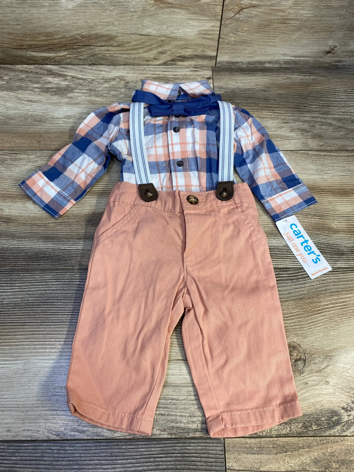 Flat lay of 4-piece plaid suspender set with navy bow tie and peach pants with white-striped suspenders on wood background