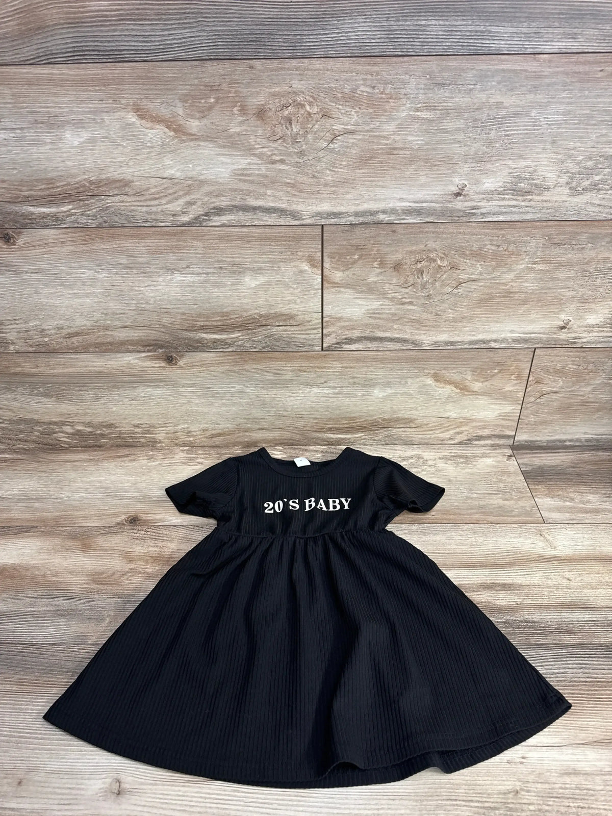 Black short sleeve toddler dress with '20'S BABY' text on wooden floor