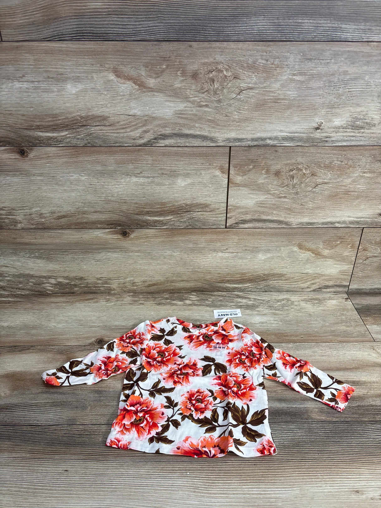 Floral long sleeve baby shirt with red and pink flowers on wooden background