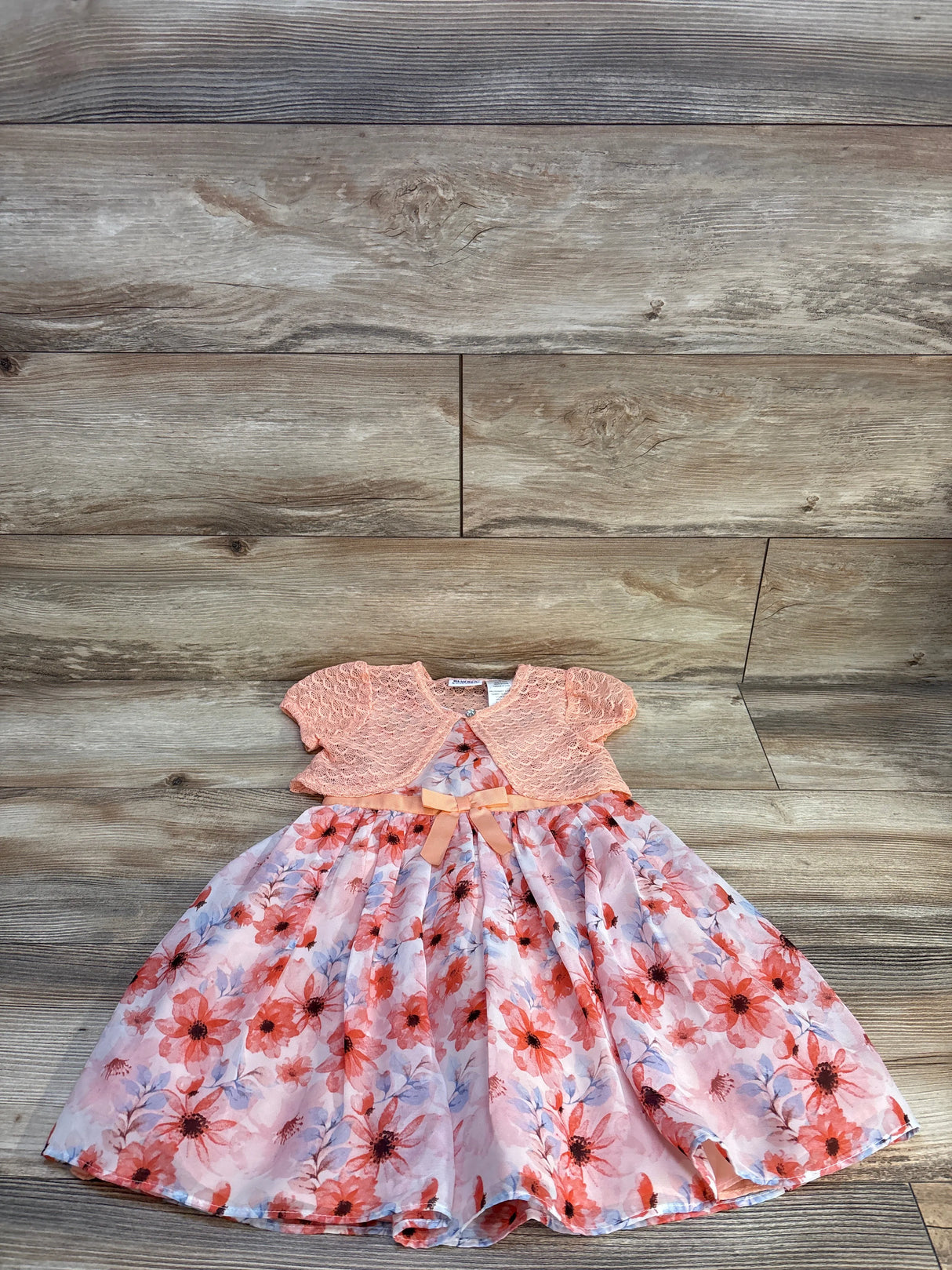 Girls' floral dress with pink lace cardigan and bow, laid on wood floor