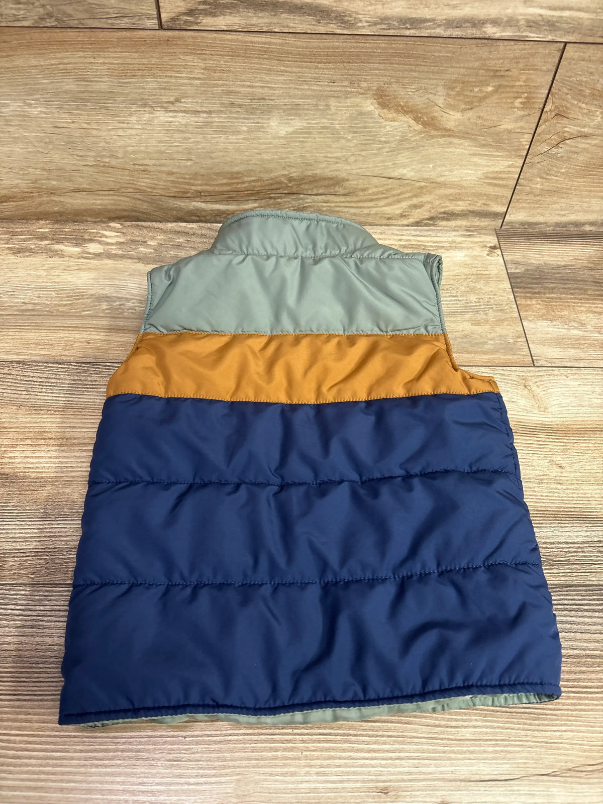 Back view of Carter’s green full-zip vest jacket, size 3T, showcasing navy and mustard quilted panels on wood flooring