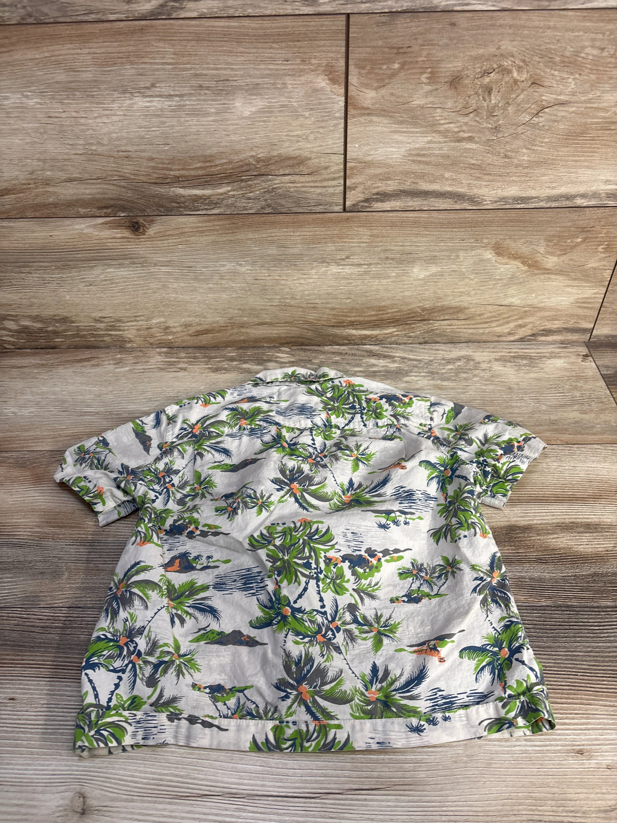 Back view of Tucker + Tate Hawaiian Dino button-up shirt in beige, size 4T, showcasing allover dinosaur print on wood flooring