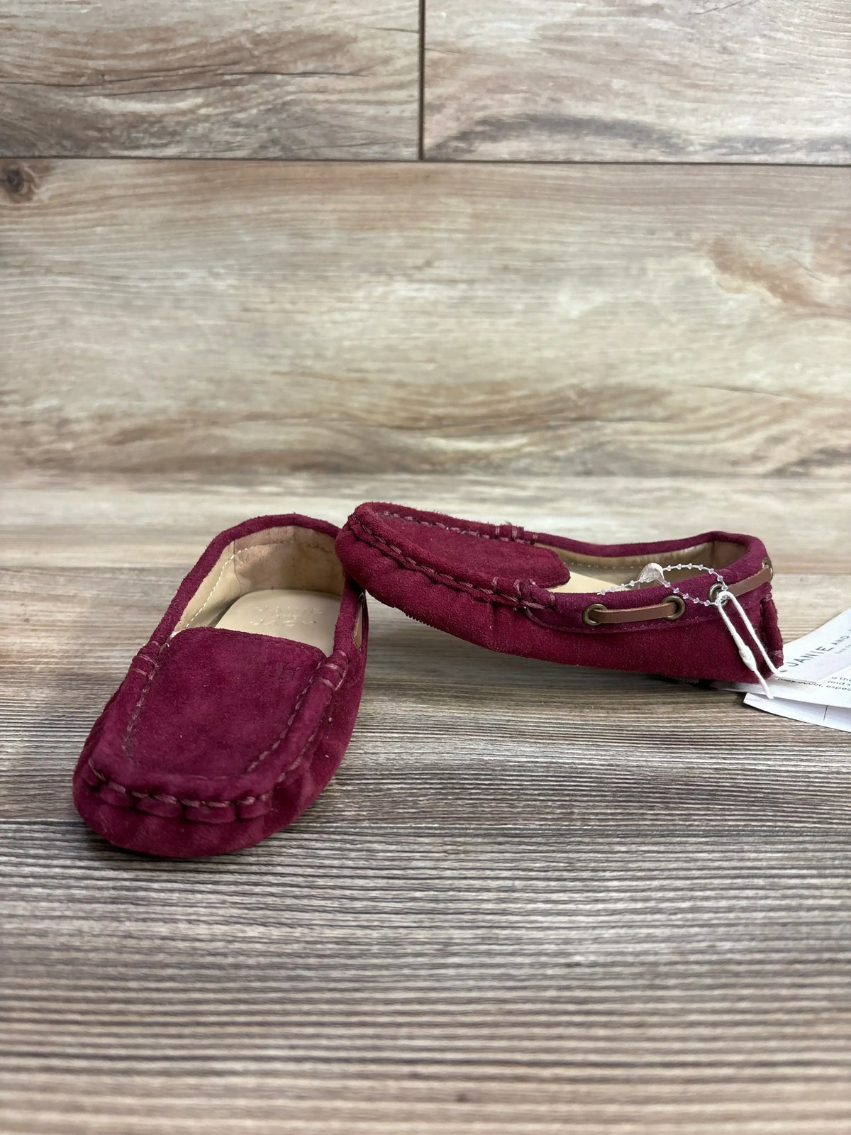 Pair of children's burgundy suede moccasin shoes on wooden floor background
