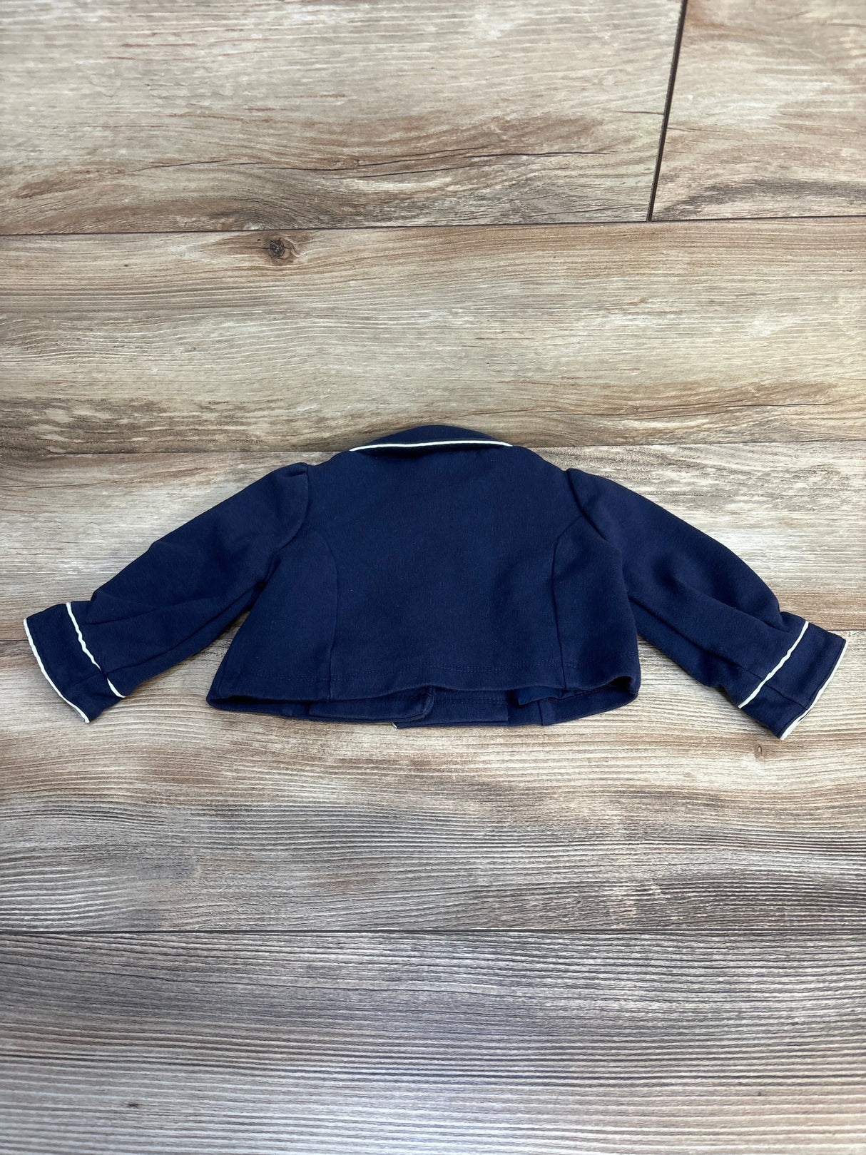 Navy blue children's blazer jacket with white trim on cuffs, displayed on wood floor