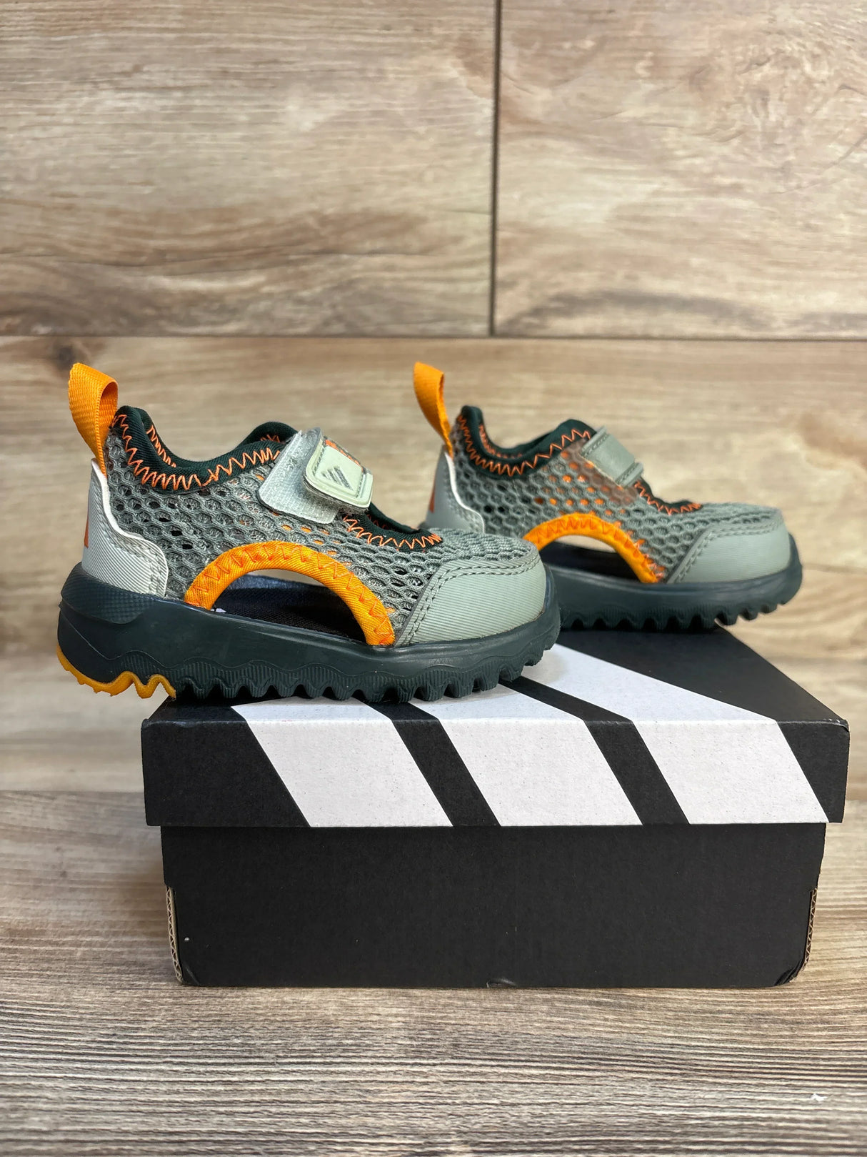 Kids' gray and orange mesh sneakers with Velcro straps on a shoebox, wooden background