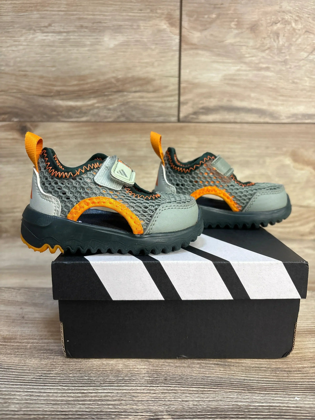 Side view of Adidas Summerflex I size 4C sandals in silver-green and orange showing mesh upper and Velcro strap on a shoebox