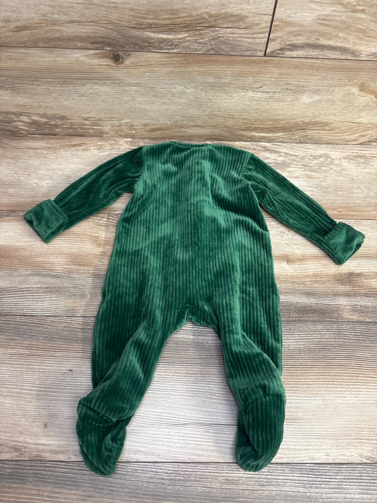 Green ribbed velour infant footed sleeper laid flat on wood floor, soft baby clothing