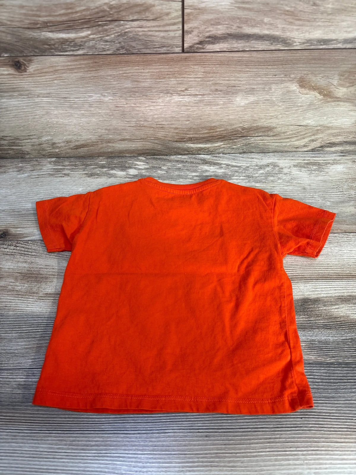 Back view of Kenzo Kids t-shirt showing solid orange cotton and crew neck, laid flat on wood