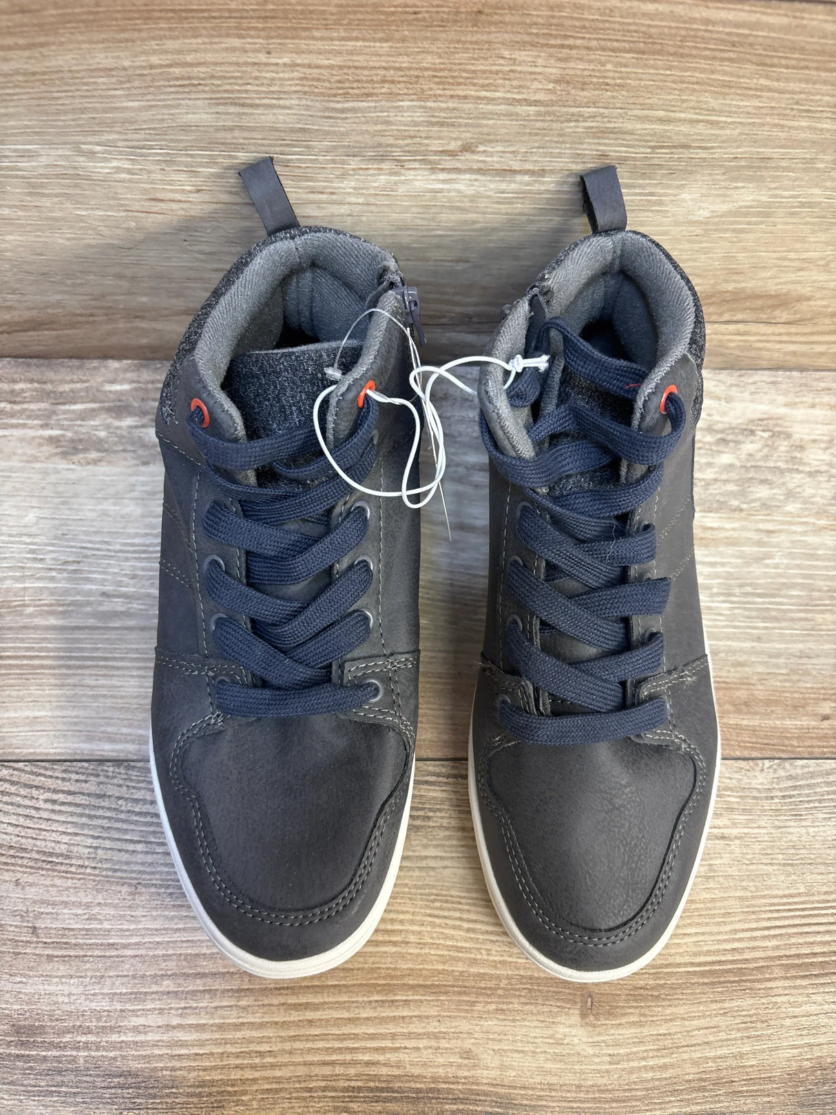 Pair of black high-top kids sneakers with navy laces on wood floor, gently used