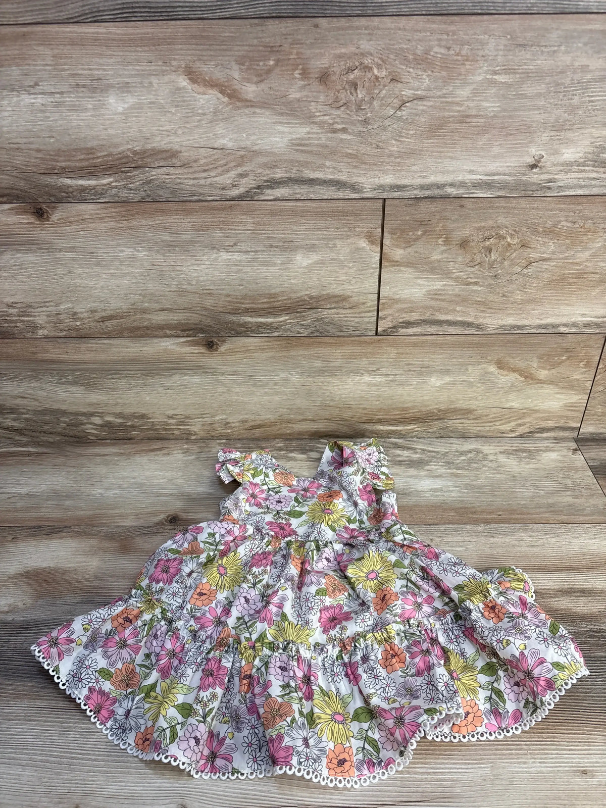 Flat lay of Rare Editions white floral toddler dress size 2T with ruffle sleeves and scalloped eyelet hem on wood background
