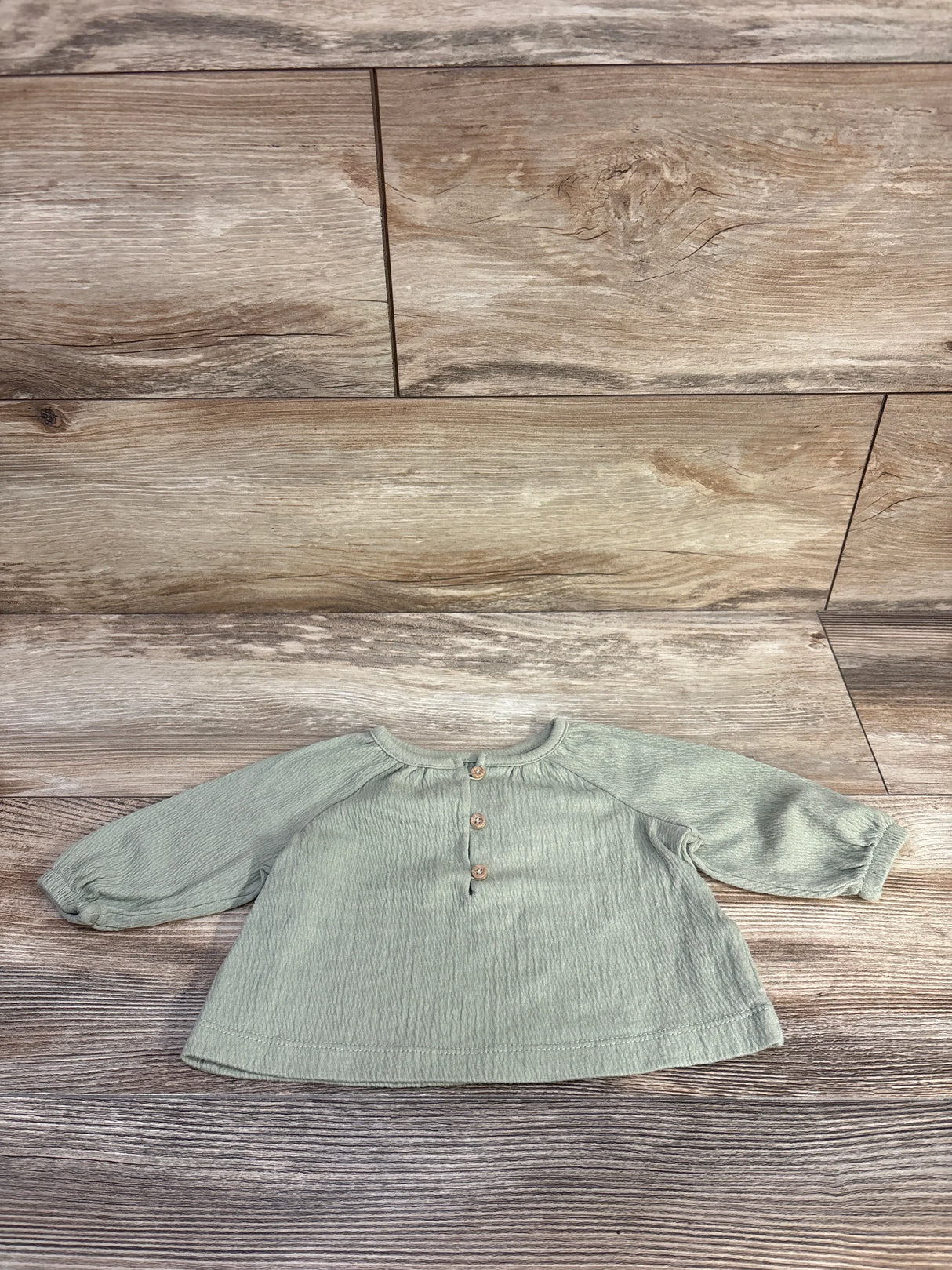 Front view of Carter's long-sleeve henley baby shirt, green 3M, showing button placket and raglan sleeves on wood background