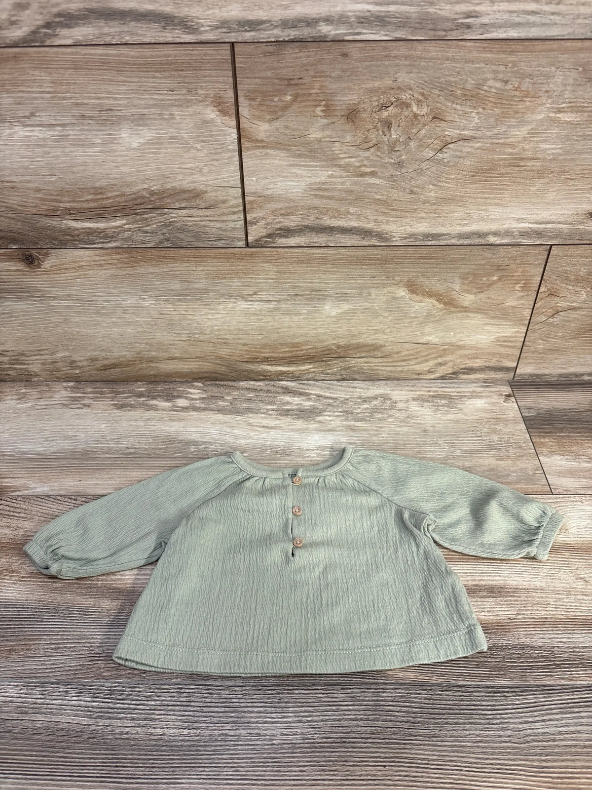 Front view of Carter's long-sleeve henley baby shirt, green 3M, showing button placket and raglan sleeves on wood background