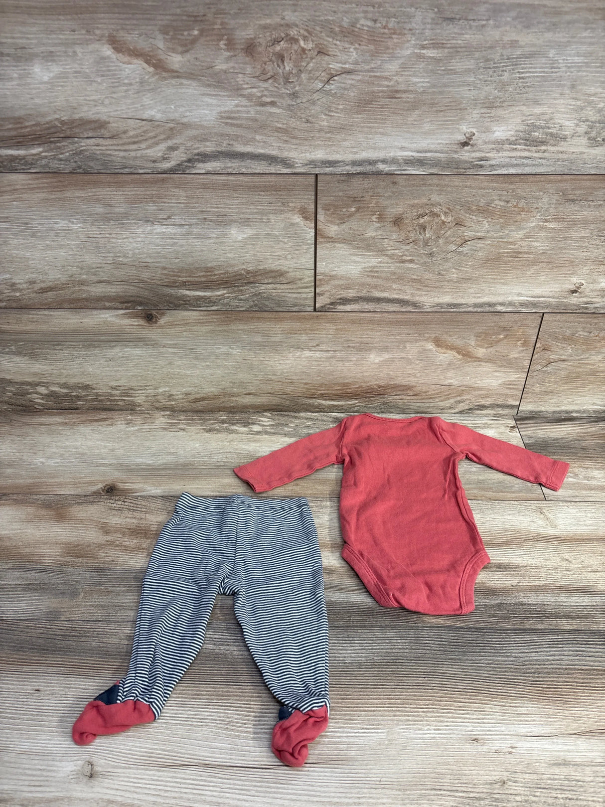 Striped baby pants with feet and a coral long sleeve baby bodysuit on wood floor