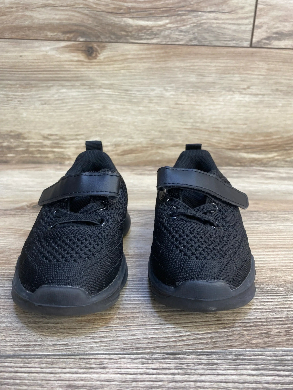Black toddler sneakers with hook and loop straps on wood floor