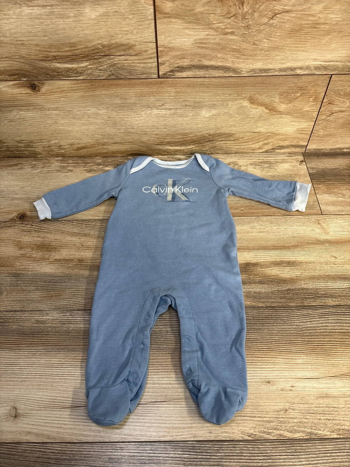 Blue Calvin Klein baby sleeper with white cuffs laid flat on wooden floor
