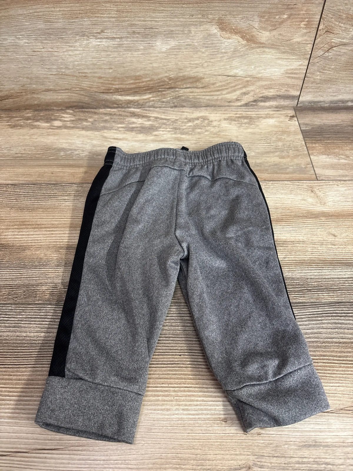 Flat lay of Jumping Beans grey toddler active joggers showing elastic waistband and black side stripe on wood floor