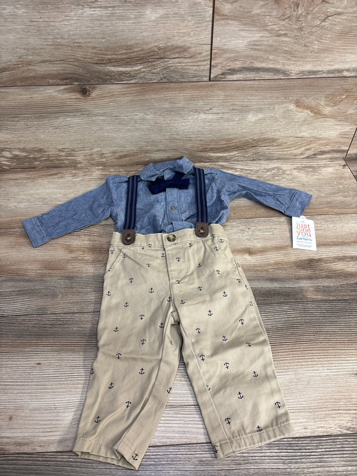 Baby boy outfit with blue shirt, navy bow tie, suspenders, and anchor print khaki pants on wood floor