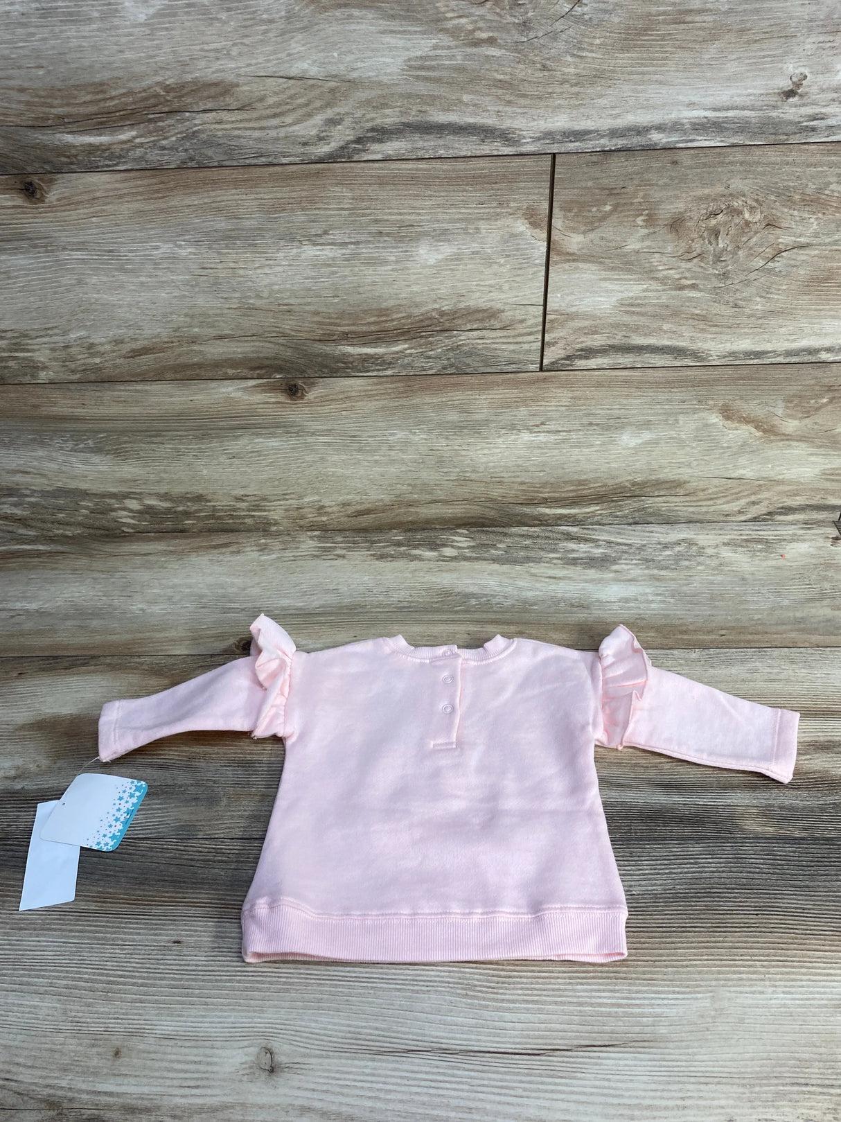 Light pink long-sleeve baby shirt with ruffle sleeves and snap buttons on wood floor