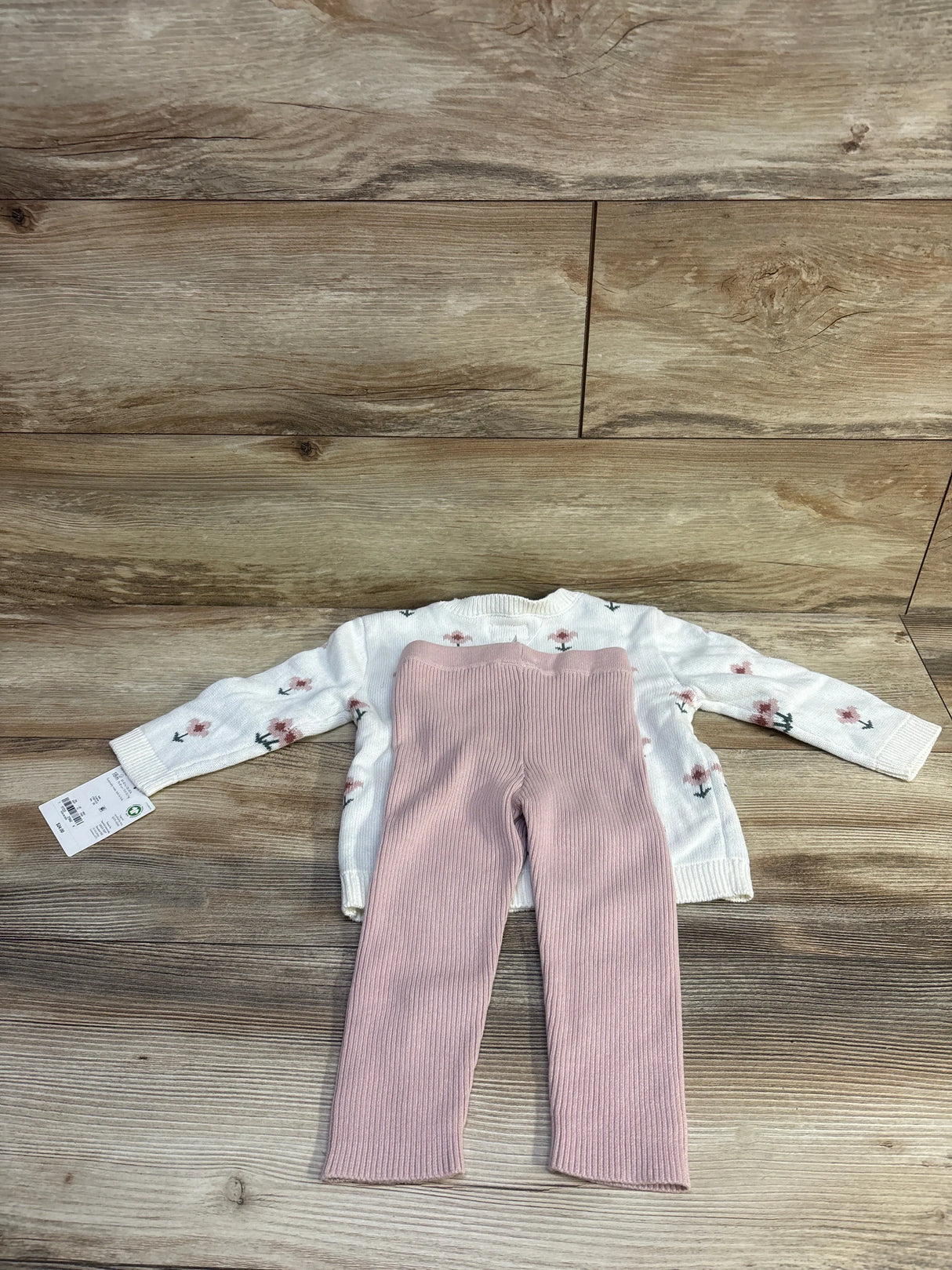 Flat lay of Little Planet organic 2-piece floral sweater set showing cream knit sweater with pink ribbed pants on wood background