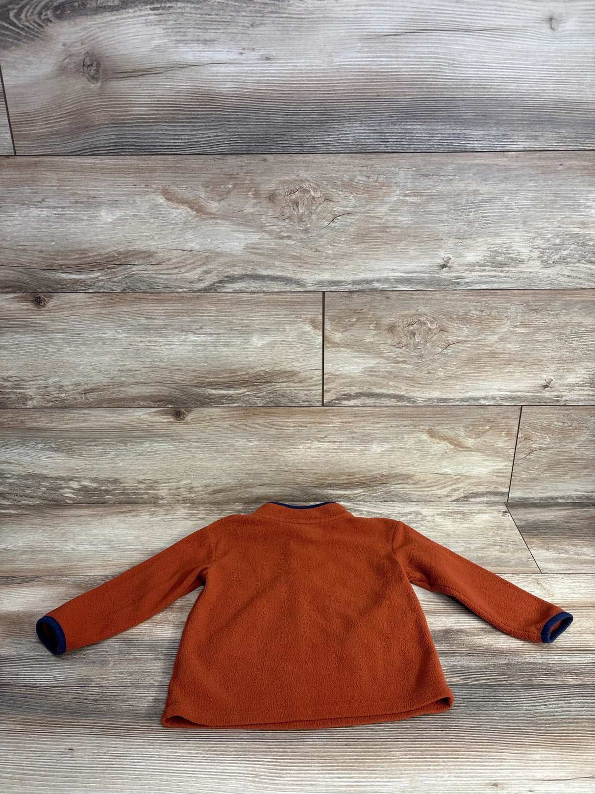 Orange fleece toddler jacket with long sleeves on wood background