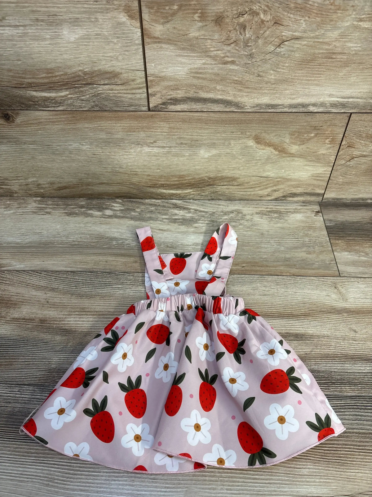 Flat lay of pink strawberry-print skirtall showing gathered elastic waist and white flower print on wood floor background