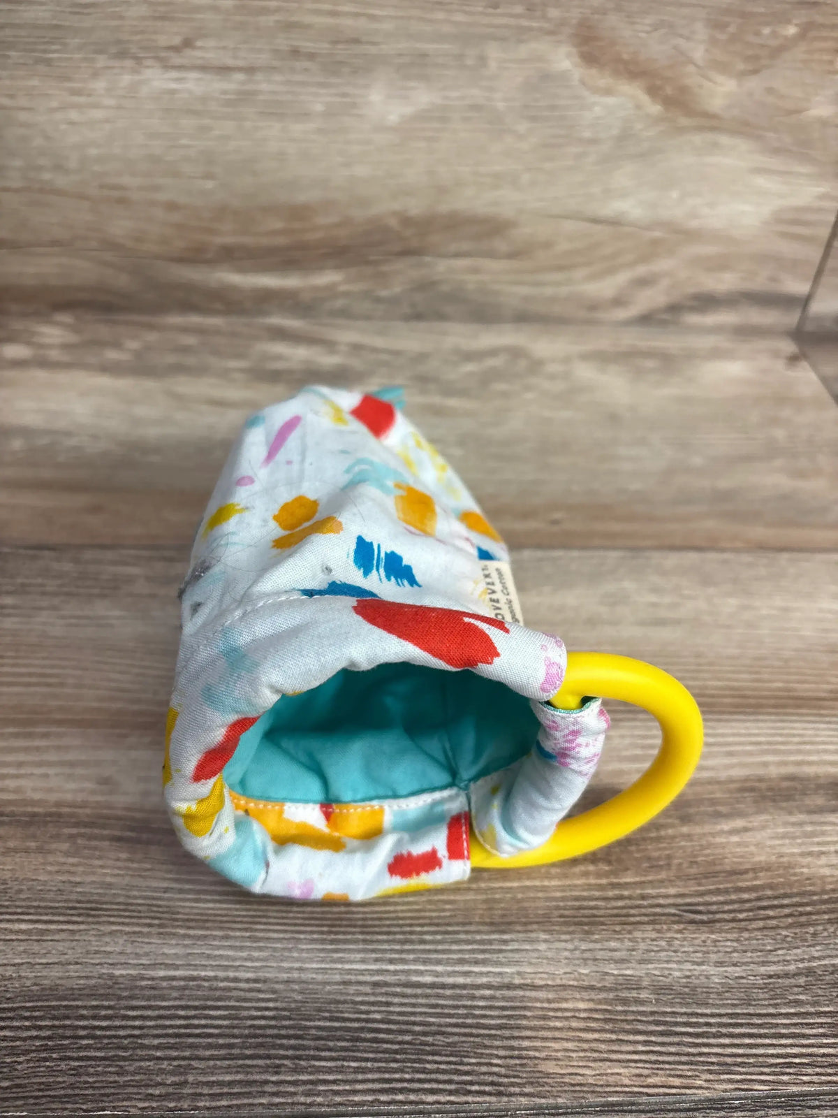Angled view of Lovevery Organic Cotton Sensory Pouch with reversible multicolor fabric and yellow teething ring on wood