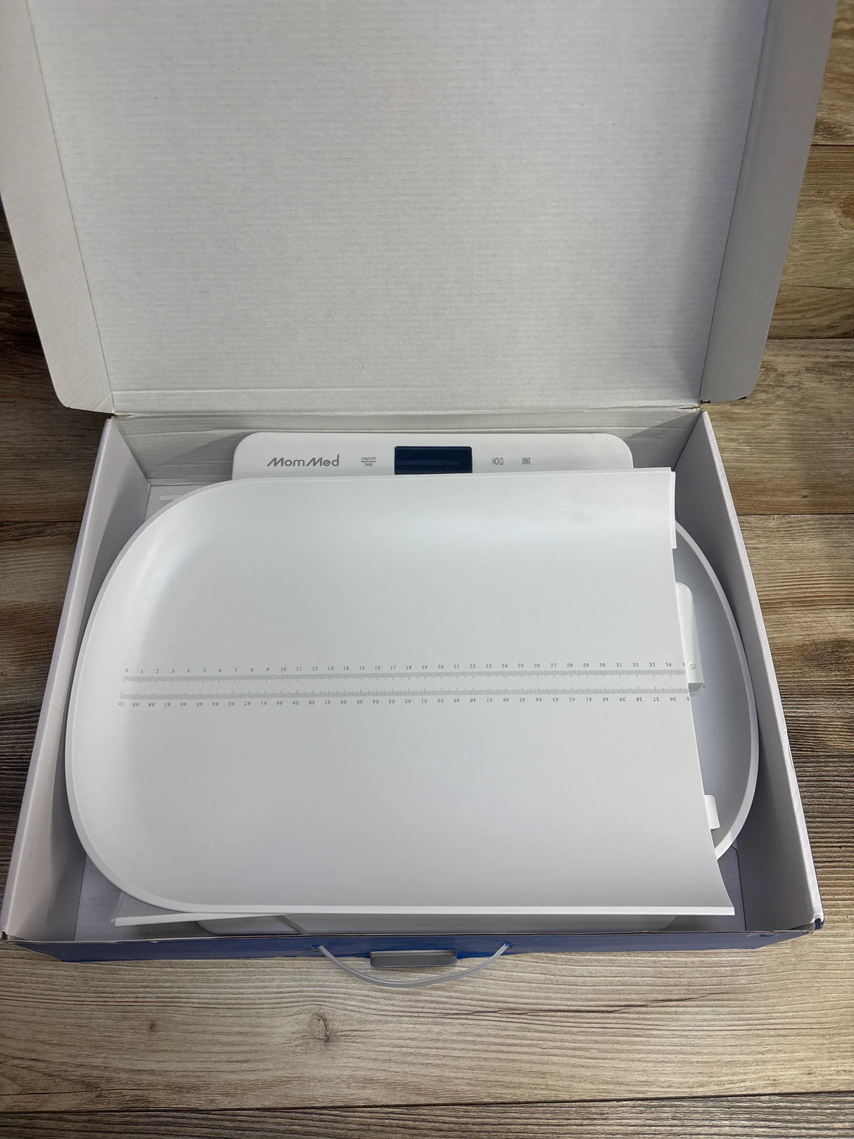 Digital baby scale with measuring tray in open box on wooden surface