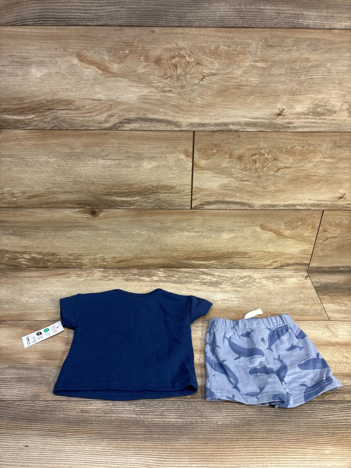 Flat lay of baby navy textured short sleeve top and light blue whale print shorts showing elastic waistband on wood background