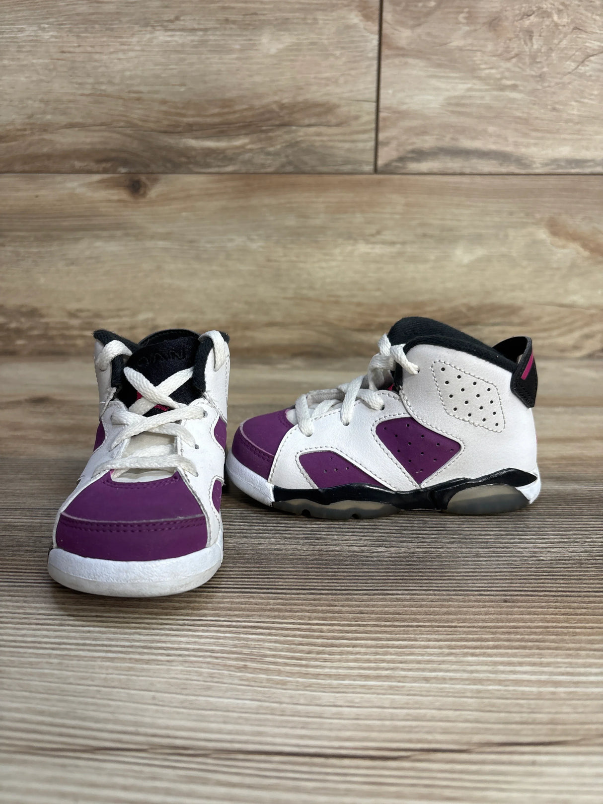 Pair of toddler high-top sneakers with white and purple panels on wooden floor