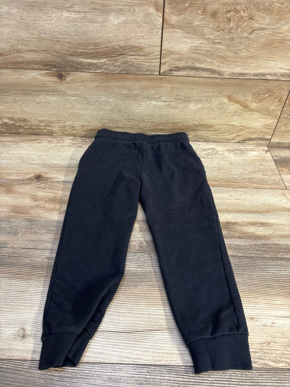 Flat lay of black Carter’s toddler joggers (size 5T) showing elastic waistband and ribbed ankle cuffs on wood floor