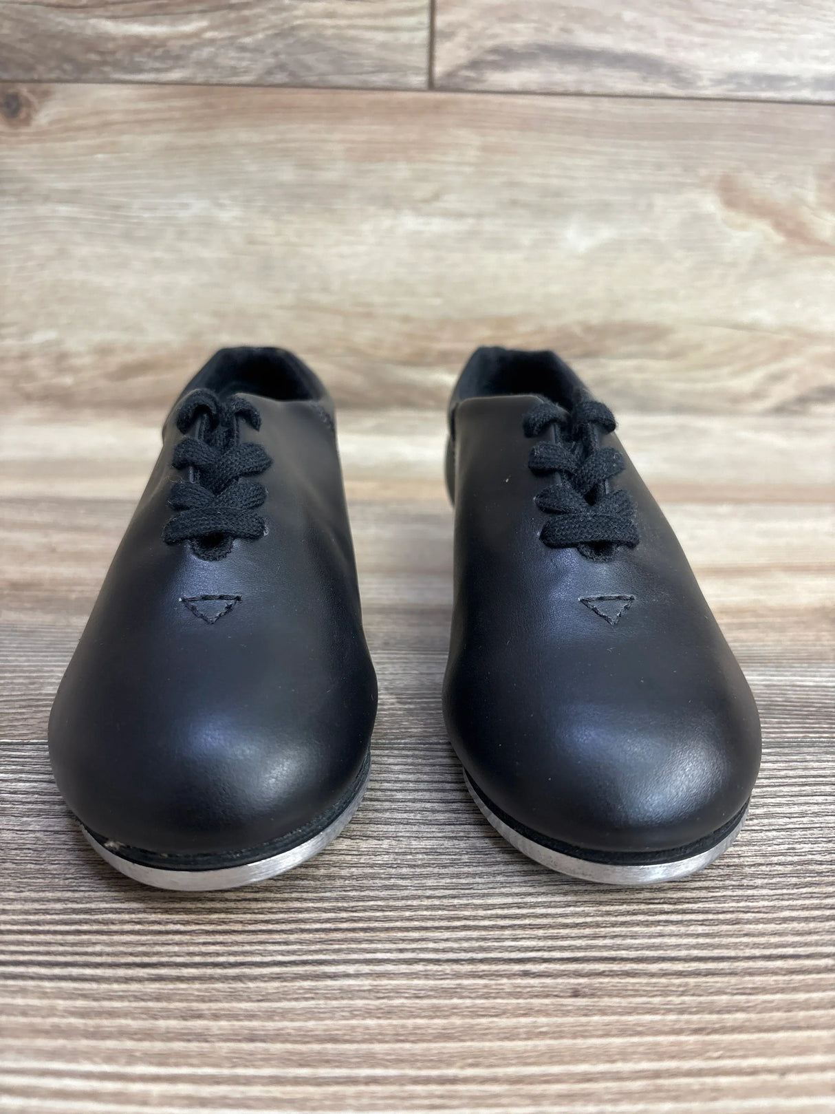 Pair of black leather tap shoes with black laces on wooden surface, children's dance footwear